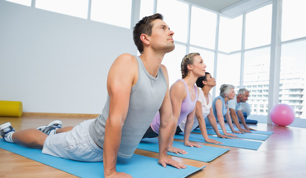 Fitness group doing cobra pose in row at the yoga class